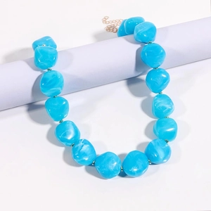Dettaglio di perle blu marmorizzate su catena dorata esposte su un supporto cilindrico