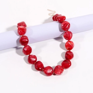Dettaglio della collana di perle rosse irregolari con trama marmorizzata e catena d'oro