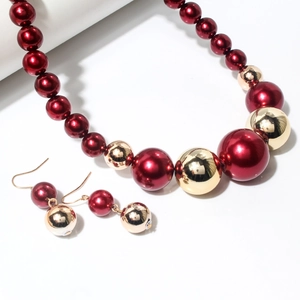 Dettaglio della collana e orecchini con perle rosse e dorate su uno sfondo bianco