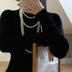 Détail d'un élégant collier de perles long multicouche porté sur un pull à col roulé noir