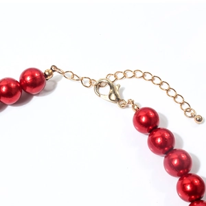 Dettaglio macro di collana con perle rosse, chiusura a moschettone dorata e catenella regolabile