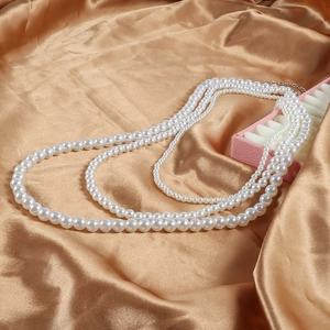 Gros plan d'un collier de perles blanches à trois rangs sur satin de couleur champagne