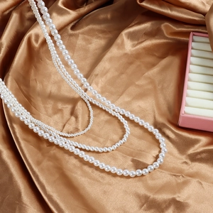 Détail d'un collier de perles blanches multicouche sur un tissu en soie dorée élégant