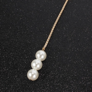 Detail of gold chain with three vertical white pearls on a black glitter background