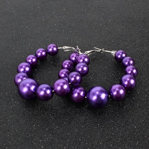 Dettaglio di orecchini a cerchio con perle sfumate viola su uno sfondo scuro lucido