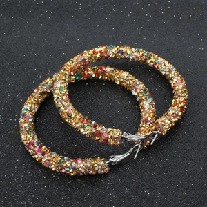 Macro view of gold hoop earrings encrusted with colorful rhinestones on black background