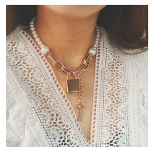 Collar de perlas moderno con colgante de candado y llave sobre camisa de encaje blanco