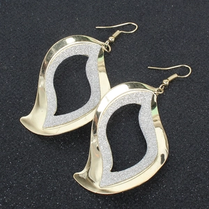 Dettaglio macro di grandi orecchini geometrici con cornice dorata e glitter argento