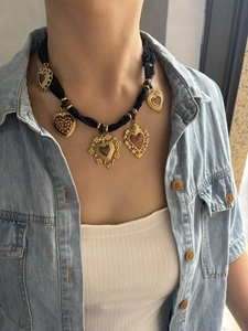 Dettaglio di cinque ciondoli a cuore dorati su una collana in corda intrecciata nera