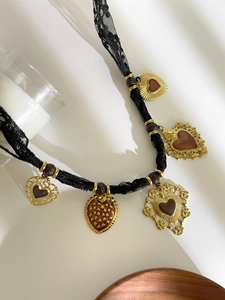Dettaglio della collana in pizzo nero con cinque ciondoli a cuore dorati e smalto marrone