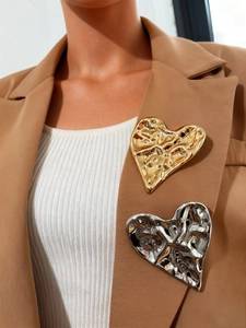 Macro detail of large irregular heart brooches in gold and silver on a camel blazer