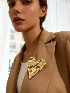 Close-up of golden wrinkled heart brooch with hammered texture on camel blazer