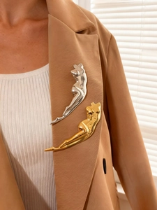 Close-up of golden and silver female body sculpture brooches on a brown suit lapel