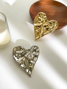 Detailed view of textured gold and silver heart-shaped brooches in irregular wavy design
