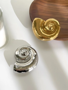 Detailed view of conch-shaped metallic brooches in gold and silver with mirror finish