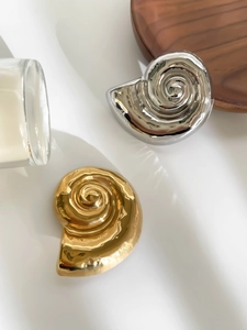 Macro view of metallic spiral shell brooch in polished gold and silver finishes