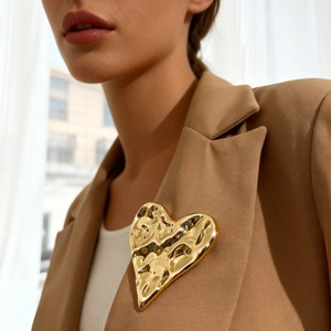 Vintage oversized gold heart brooch with hammered texture on a stylish beige blazer