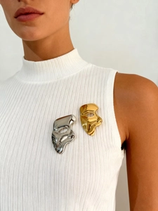 Detail showing polished gold and silver mask brooches on white knit fabric garment