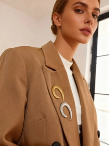Detail of silver and gold crescent brooches with hammered texture on a brown blazer
