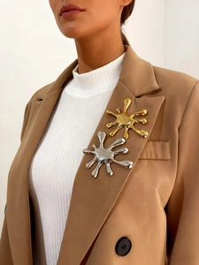 Macro view of gold and silver liquid splatter brooches on a dark brown suit lapel