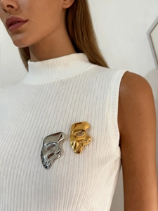 Close-up of gold and silver mask-shaped brooches on a white knitted vest fabric