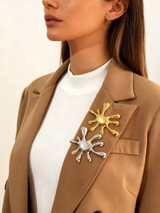 Close-up of gold and silver irregular liquid-style firework brooches on a blazer