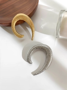 Macro view of textured hammered U-shaped metal brooches in gold and silver finish