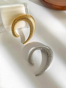 Macro detail of U-shaped metal earrings with hammered texture in gold and silver finishes