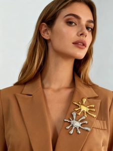 Macro shot of silver and gold firework brooches on a brown blazer lapel with mirror finish