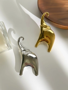 Macro shot of minimalist gold and silver elephant brooches on a wooden tray
