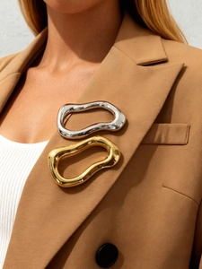 Detail of irregular wave-shaped gold and silver brooches pinned on a camel blazer lapel