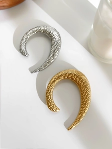 Detail of gold and silver U-shaped textured metal brooches with hammer finish