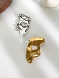 Polished silver mask brooch with pin clasp detail on a minimalist white background