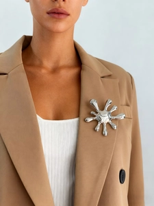 Detail of silver liquid metal firework brooch on khaki blazer lapel