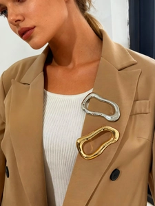 Close-up of gold and silver irregular abstract brooches on a khaki blazer lapel