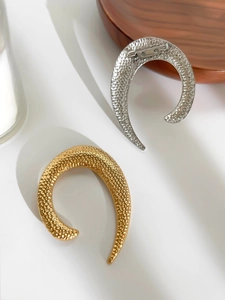 Detail of gold and silver U-shaped metal brooches with handmade hammered texture surface