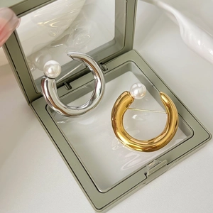 Dettaglio di spille a forma di C in oro e argento con perle bianche in una scatola gioielli