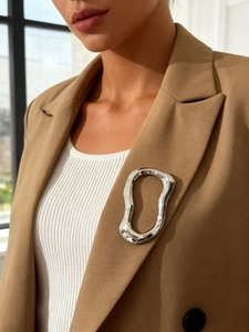 Close-up of a silver fluid geometric brooch on a camel blazer lapel showing mirror polish