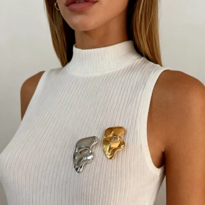 Artistic theater mask brooches in gold and silver finish on white ribbed turtleneck top