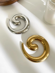 Macro detail of twisted spiral snail brooches in polished gold and silver metal finishes