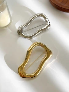 Macro detail of polished irregular wave brooch showing the secure pin back and metallic texture