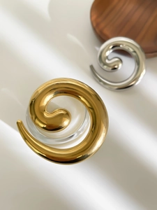 Macro shot of minimalist twisted spiral metal brooches in polished gold and silver finishes