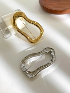 Detail of irregular wave brooches in gold and silver showing metallic texture and pin back