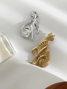 Détail des broches chat en or et argent avec textures géométriques sur soie blanche
