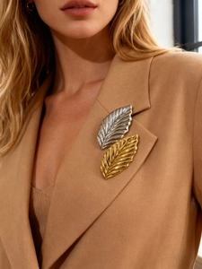 Detailed view of gold and silver leaf brooches on a camel blazer lapel showing fine texture
