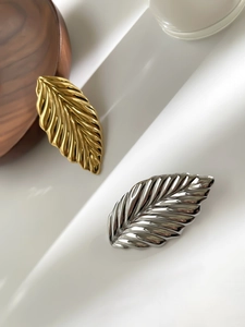 Detail of gold and silver leaf brooches with textured metal veins on a white display