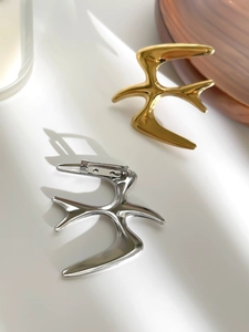 Detailed view of polished swallow bird brooches in gold and silver finish with pin clasp