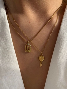 Detail van dubbellaagse gouden ketting met rozenkooi en stervormige sleutelhanger