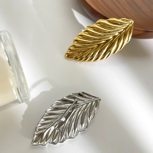 Elegant gold and silver leaf brooches with wavy texture on a minimalist white background