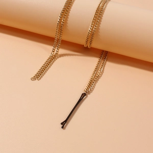 Elegante goldene Haarkette mit schwarzer Haarnadel auf minimalistischem Pfirsich-Hintergrund